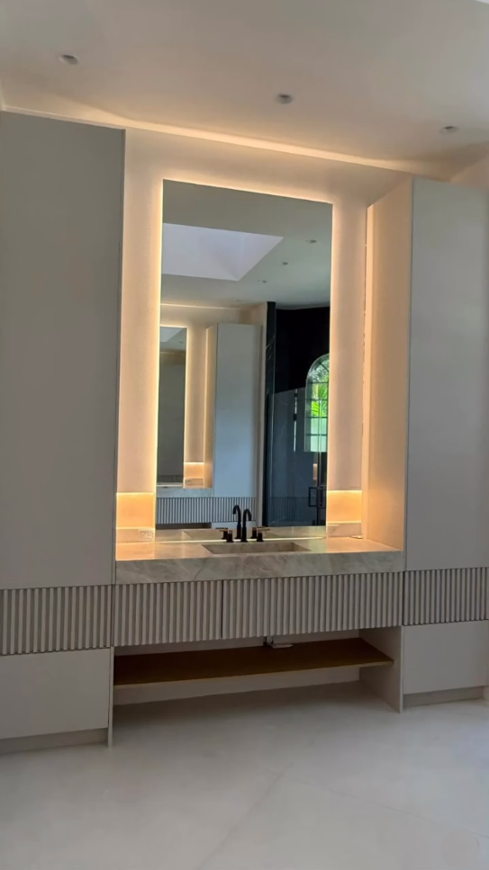 Modern luxury bathroom with a large backlit LED mirror, marble countertop, and fluted grey cabinetry.