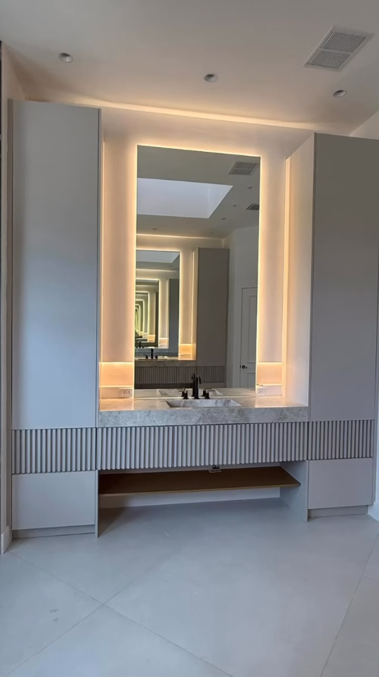 Modern luxury bathroom with a large backlit LED mirror, marble countertop, and fluted grey cabinetry.