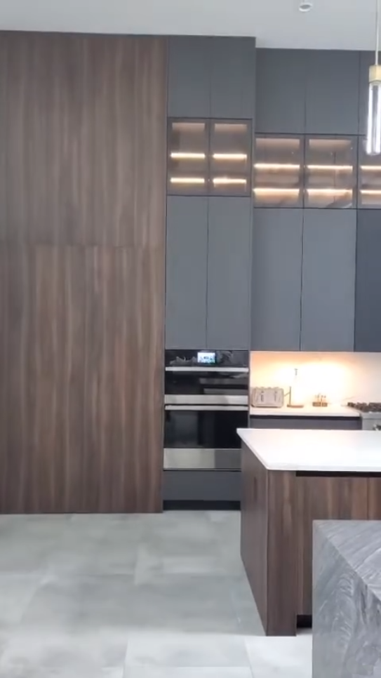Modern luxury kitchen wall with floor-to-ceiling charcoal and wood cabinetry, backlit display cases, and integrated double ovens.