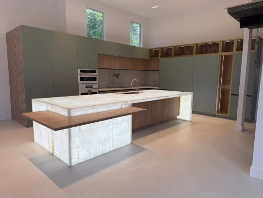 Luxury kitchen design with backlit onyx waterfall island, custom olive green cabinets, and integrated LED shelf lighting.