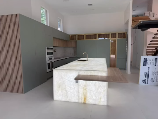 Luxury kitchen design with backlit onyx waterfall island, custom olive green cabinets, and integrated LED shelf lighting.