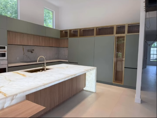 Luxury kitchen design with backlit onyx waterfall island, custom olive green cabinets, and integrated LED shelf lighting.