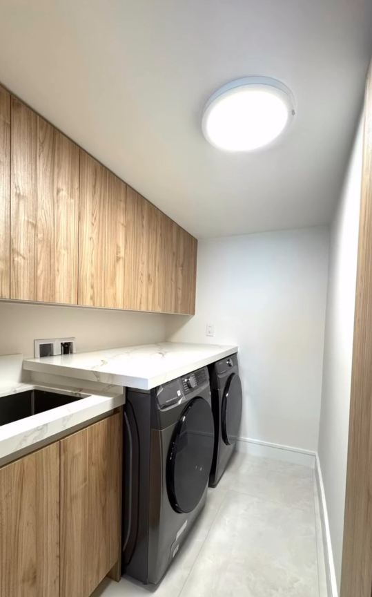 Modern laundry room with custom wood cabinets, marble folding counter, and dark grey front-load laundry machines.