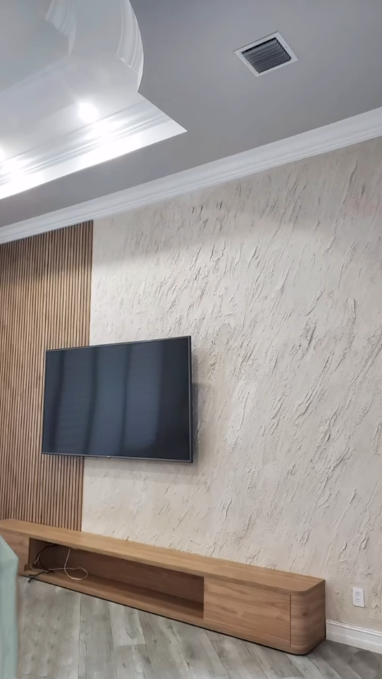 Modern living room with a textured plaster feature wall, vertical wood fluted paneling, and a custom curved wood media console.