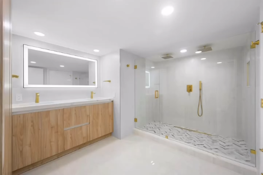Modern luxury bathroom with a double wood vanity, LED-illuminated mirror, and a glass-enclosed shower with golden hardware.