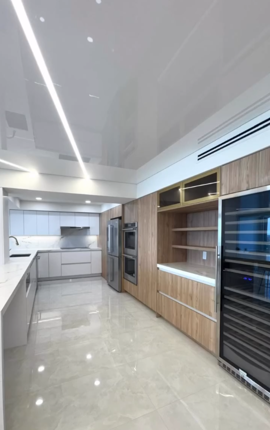 Minimalist kitchen design with stretch ceiling, architectural LED lighting, and integrated wine storage.