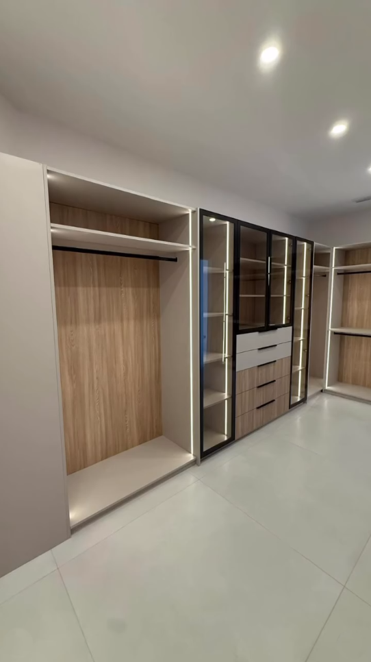 Modern custom walk-in closet with integrated LED lighting, light wood finishes, and glass-front display cases.
