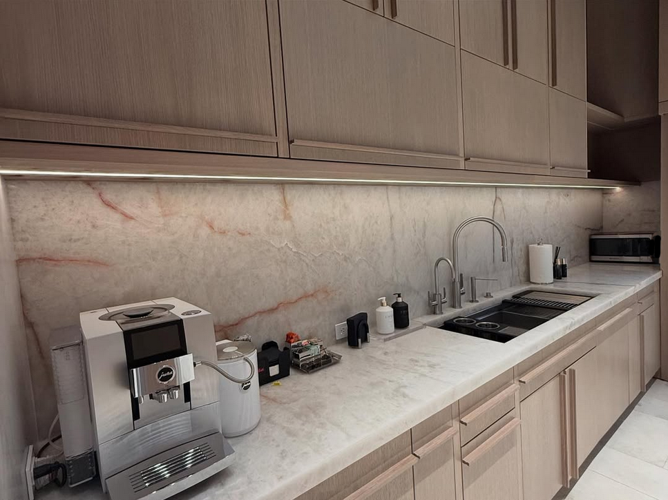 Modern kitchen workstation featuring marble waterfall countertops, pink marble backsplash, professional espresso station, and integrated sink.