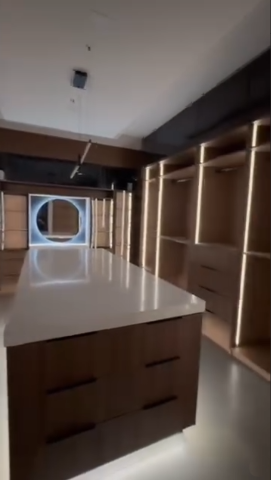 Modern walk-in closet featuring integrated vertical LED lighting, dark wood cabinetry, and a large central storage island.