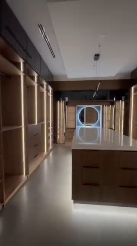 Modern walk-in closet featuring integrated vertical LED lighting, dark wood cabinetry, and a large central storage island.
