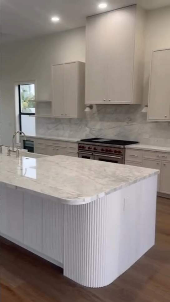Large white luxury kitchen with a curved fluted island, marble countertops, and professional-grade appliances.