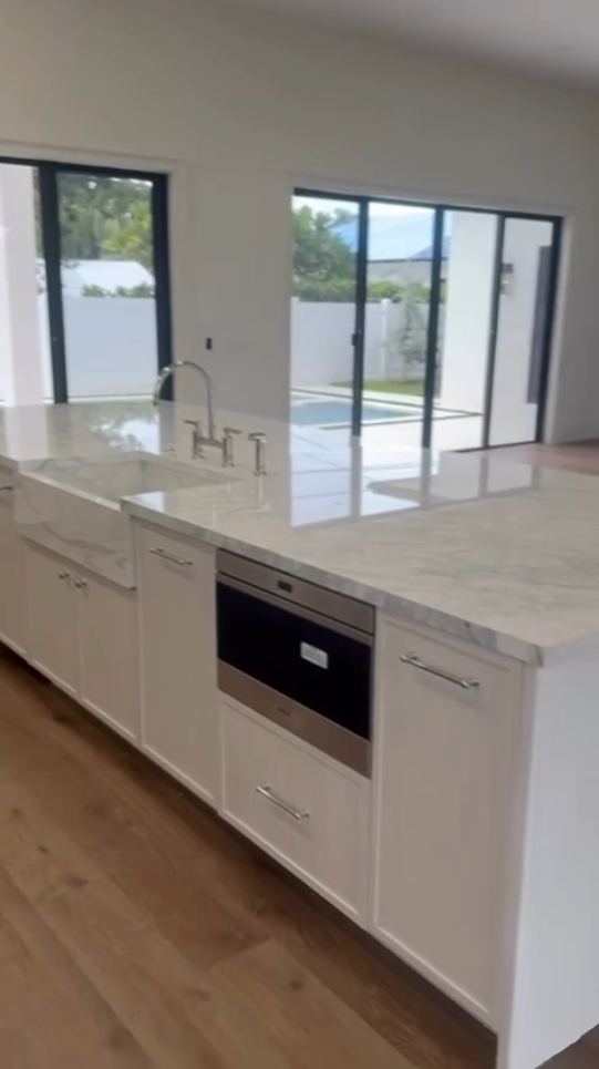 Large white luxury kitchen with a curved fluted island, marble countertops, and professional-grade appliances.