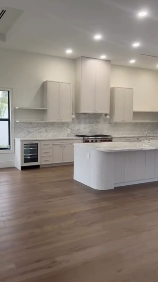 Modern white kitchen with marble countertops, a custom fluted kitchen island, and built-in wine refrigeration.