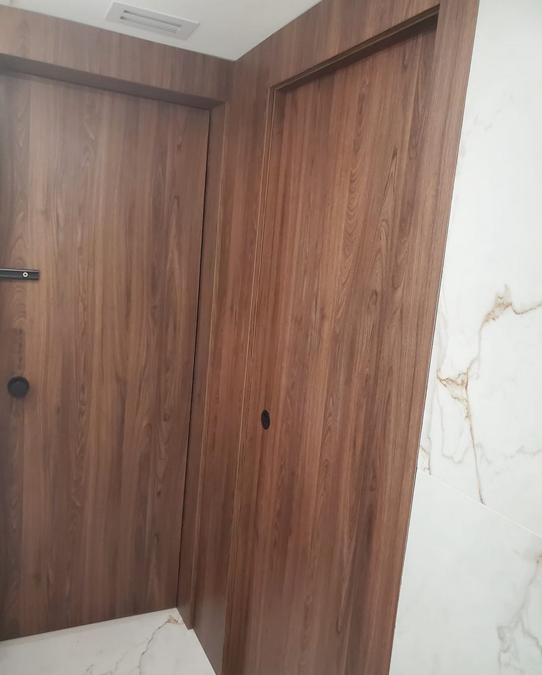 Luxury interior featuring custom flush-mount dark wood doors integrated into matching wall panels beside a white marble accent wall.