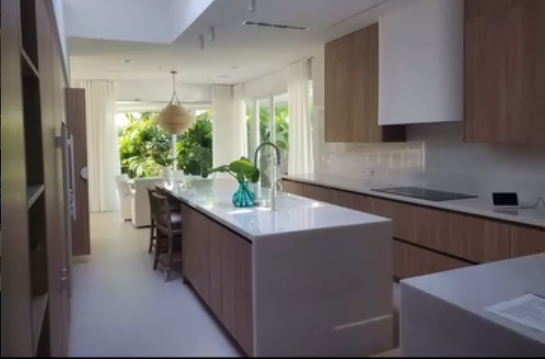 Modern kitchen and dining space featuring wood cabinetry, a white waterfall island, and views of the garden.