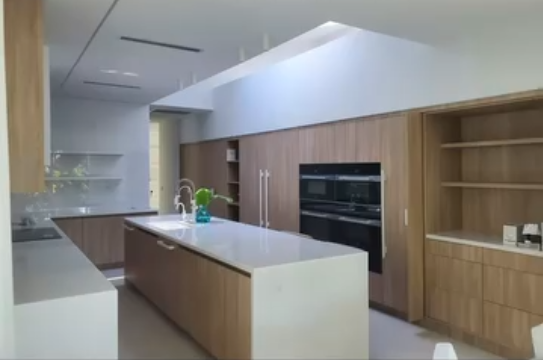 Modern kitchen design with light wood custom cabinetry, a white waterfall island, and a large skylight.