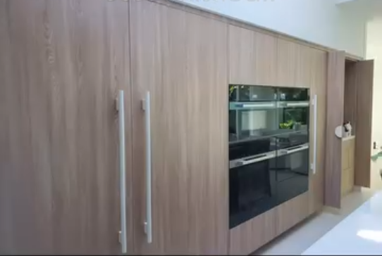 Luxury custom kitchen cabinetry with integrated wall ovens, floor-to-ceiling wood panels, and modern hardware.