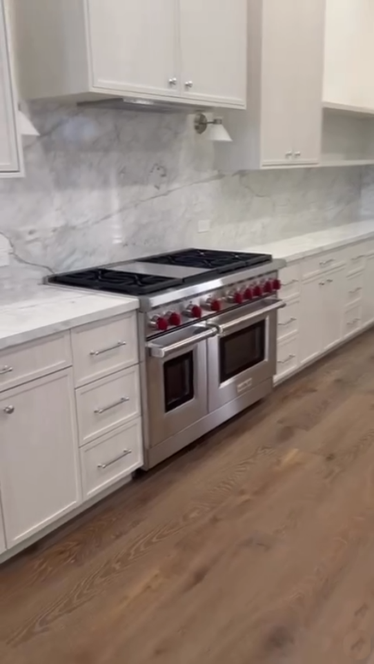 Luxury white kitchen featuring a professional stainless steel range, marble slab backsplash, and white cabinetry with chrome hardware.